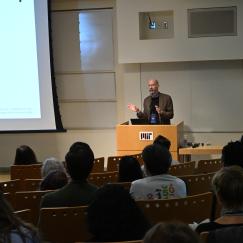 Earl Miller stands at a podium in MIT's Building 46, gesturing as he speaks to a room full of people.