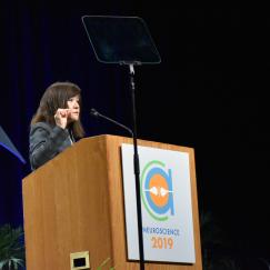 Li-Huei Tsai stands at the SfN podium gesturing as she gives her talk 