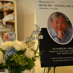 A bouquet of flowers sits in the foreground of two large photos on easels of Susumu Tonegawa at different stages of his career