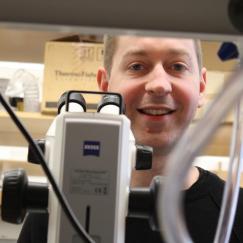 Steve Flavell looks up from a microscope in his lab and smiles