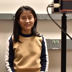 Linlin Fan stands in her lab with microscope equipment in the foreground.
