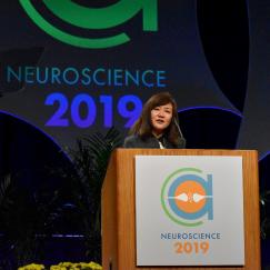 Li-Huei Tsai speaks from the podium with a huge Neuroscience 2019 sign behind her