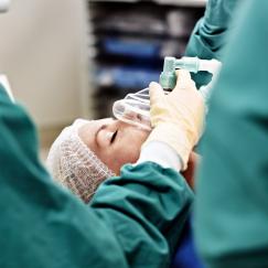 A member of a surgical staff holds a mask on the face of an unconscious patient in an operating room