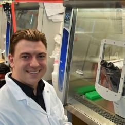Jonathan Palmiero sits before a fume hood with a microscope inside. His image then blurs into one of Laura Neal seated at a lab bench