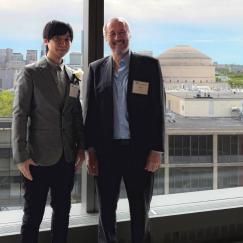 Takato Honda and Matt Wilson stand side by side and smile in front of a window overlooking other campus buildings including the Great Dome.