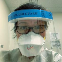 A woman wears a mask, a paper gown and a plastic face shield
