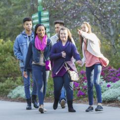 A teen girl with down syndrome walks through a park with friends