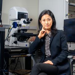 Gloria Choi looks directly at the camera as she sits at a microscope station in her lab
