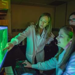 Sara Prescott points to a scientific image on a monitor in a lab as two students look on.